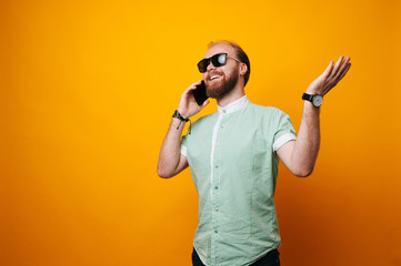 Photo of handsome excited man expressing surprise on face and gesturing while speaking on telephone over yellow background