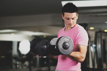 Young and strong man using dumbbells at the gym. Toned image