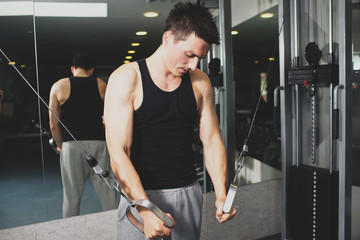 Young strong man doing exercises on the simulator at the gym. Toned image