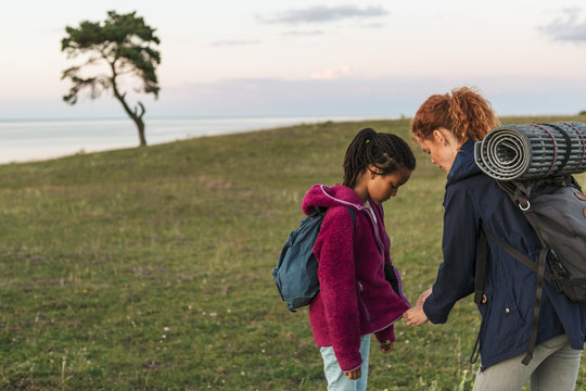 Woman zipping jacket on daughter at field during sunset