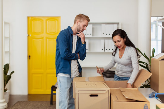 Young businessman looking at businesswoman opening cardboard box at office