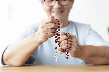 Close-up of smiling elderly person holding rosary with cross. Focus on hands