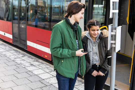 Smiling multi-ethnic teenagers standing on sidewalk against bus in city