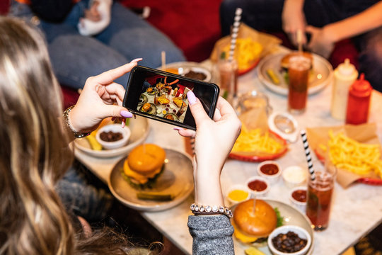 Cropped image of teenage girl photographing food and drinks served on table at restaurant