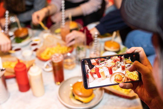 Cropped image of teenage boy photographing food and drinks served on table at restaurant