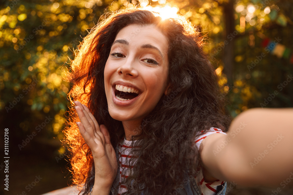 Sticker Closeup photo of joyous curly woman 18-20 taking selfie photo outdoor, during walk in park on sunny day