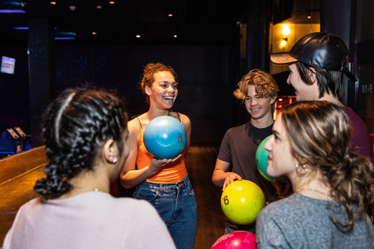 Cheerful multi-ethnic teenagers talking while holding bowling balls
