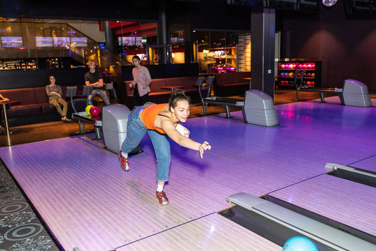 Friends looking at teenage girl throwing ball on parquet floor at bowling alley