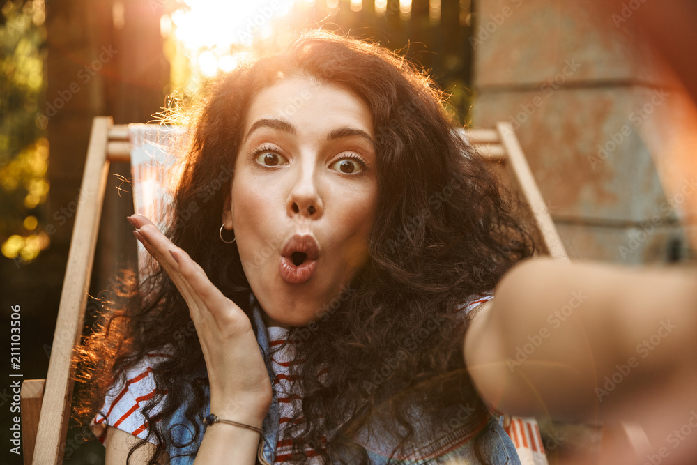 Poster picture of attractive joyful girl 18-20 looking at camera emotionally, while taking selfie photo dur