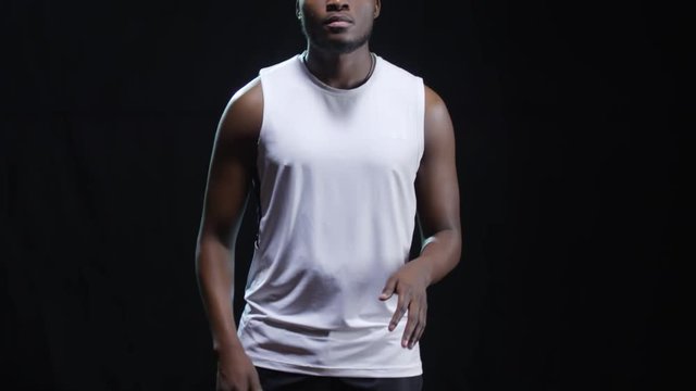 Studio shot with tilt up of confident basketball player standing isolated on black background and dribbling ball, then throwing it towards camera