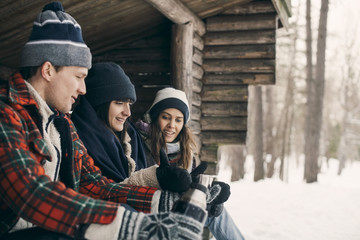 Man giving drink to female friends while sitting at log cabin during winter