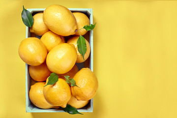 Yellow lemons in a box on a yellow background.  The view from the top. Space for text, copy space