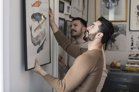 Two men hanging picture on wall