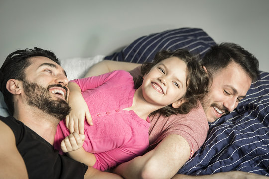 Cheerful daughter playing with fathers on bed in bedroom at home