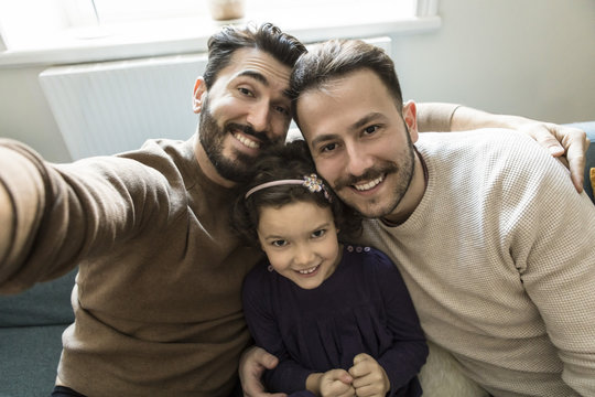 Smiling fathers and daughter taking selfie while sitting on sofa in living room at home