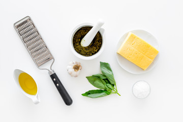 Ingredients for pesto sauce. Cheese, garlic, green basil, olive oil, salt near grater and mortar on white background top view