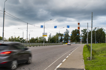 Fototapeta na wymiar Cars drive on city road. Motion blur. Pointers and road signs on cross. Overcast. Storm rain clouds in sky.