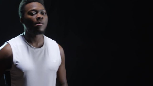 Studio shot with tilt down of serious black basketball player training isolated on black background: he catching ball and dribbling, then passing it back