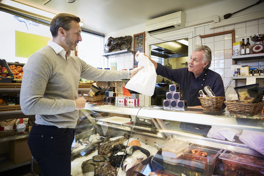 Male sales clerk handing over bag to customer at counter in store
