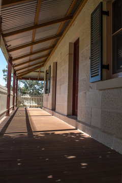 Outdoor verandah patio deck of sandstone brick cottage with picket fence in sunshine
