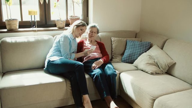Elderly grandmother and adult granddaughter with smartphone at home.