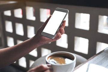 Mockup image of a woman's hand holding white mobile phone with blank desktop screen and coffee cup in cafe