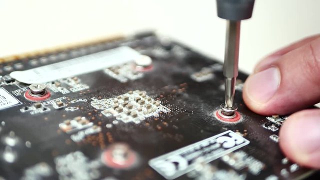 Hands of the master in the service center for computer repair screw the screw with a screwdriver on circuit board. Computer repair. Concept of computer hardware, repairing, upgrade and technology