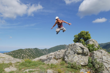 Man jumping from rock and flying in blue sky with beautiful mountain background, extreme hiking