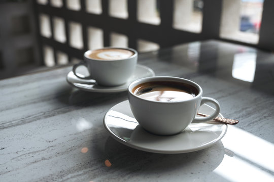Closeup image of two white cups of hot coffee on table in cafe