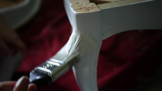 A woman paints a old antique chair with a new coat of white paint