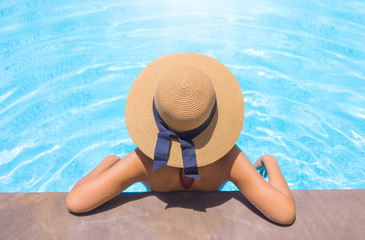 Woman with brown hat relaxing in swimming pool with blue water during a sunny day , holiday concept
