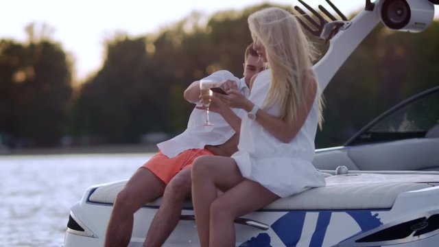 Luxury vacation on yacht on lake. Young people boating on yacht at sunset. Love couple relaxing with glass of wina on boat at sunset. Romantic dating outdoors at sunset