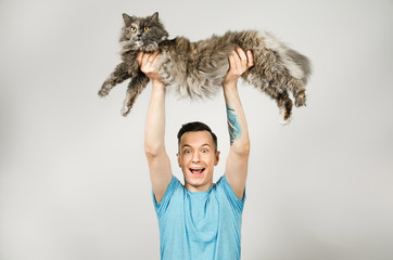 Young guy holds gray Britain cat on light gray background.