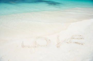 Sign love at sand beach with ocean wave crystal turquoise water. Romantic place perfect date or propose. Sand beach resort in Antigua loved by tourists. Romantic vacation ocean coast