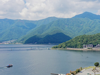 Scenery of Lake Kawaguchi, the biggest lake of Fuji five lakes, with a ferry boat and an overwater bridge crossing the lake and mt Kurodake on the background, famous tourist destination in Japan
