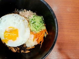 Korean food style, Top view of Rice is topped with seasoned vegetables, meat and side up fried egg on top in a black  bowl on wooden table, Space for text in template, Bibimbap is korea traditional