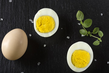 Slices of boiled hard eggs on a dark slate with green oregano