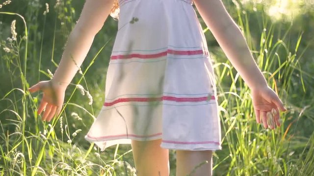 Girl, wearing summer clothes, walking in park, touching green grass with hands