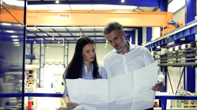 Industrial man and woman engineers looking at blueprints.