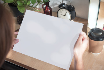hand showing blank paper A4 flyer for mockup template design logo branding on wooden background.
