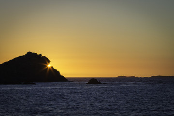 Naklejka na ściany i meble Coucher de soleil en mer derrière un rocher