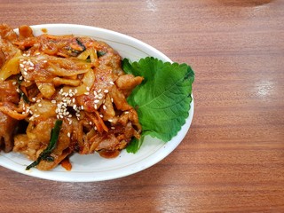 Korean food style, Top view of spicy stir fried pork  on white plate, Space for text in template, Jeyuk bokkeum is korea traditional on wooden table