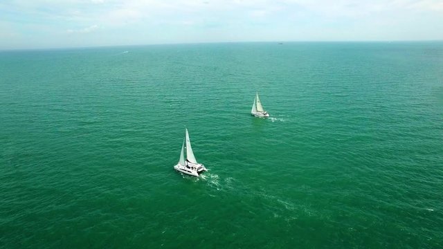 Aerial cinemagram of two beautiful sailboats - one sailing across the sea and another static
