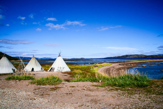 Three lavvu, or traditional lappish yurts (reindeer skin tents) used by the indigenous Sami people sit next to a lake in near Alta in the Finnmark region of northern Norway and Lapland on a summer day