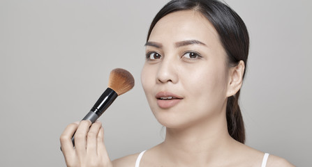 Asian woman with soft skin holding makeup brush