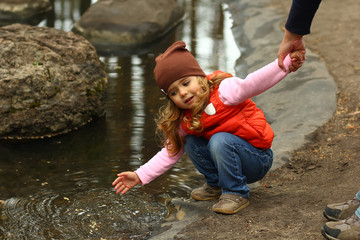 Toddler girl checking water in the park pond