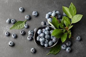Fresh blueberries with leaves on branch. Black stone background, top view.