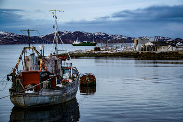 An old decaying boat floats on the calm, cold waters of the small fishing town of Aasiaat in Disko Bay, West Greenland