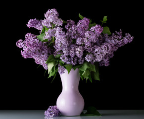 Fresh bouquet of lilac in vase isolated on black