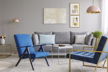 Two blue armchairs and a gray sofa standing in a living room interior with golden decorations. Real photo - obrazy, fototapety, plakaty